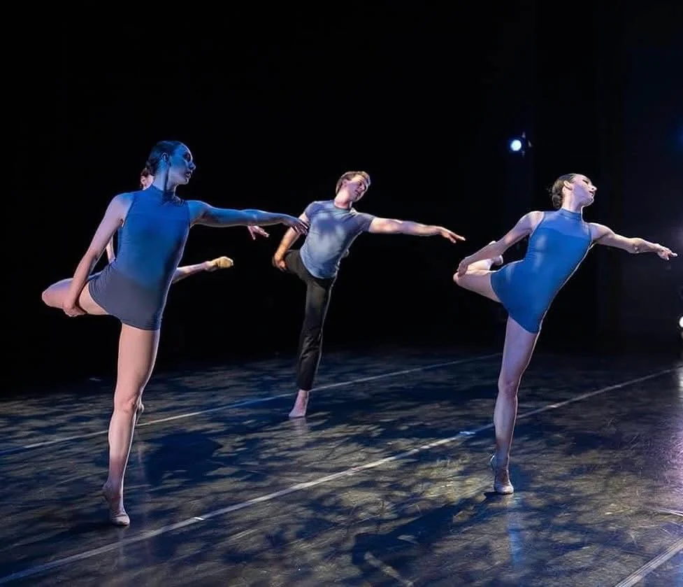 Three dancers performing under blue stage light